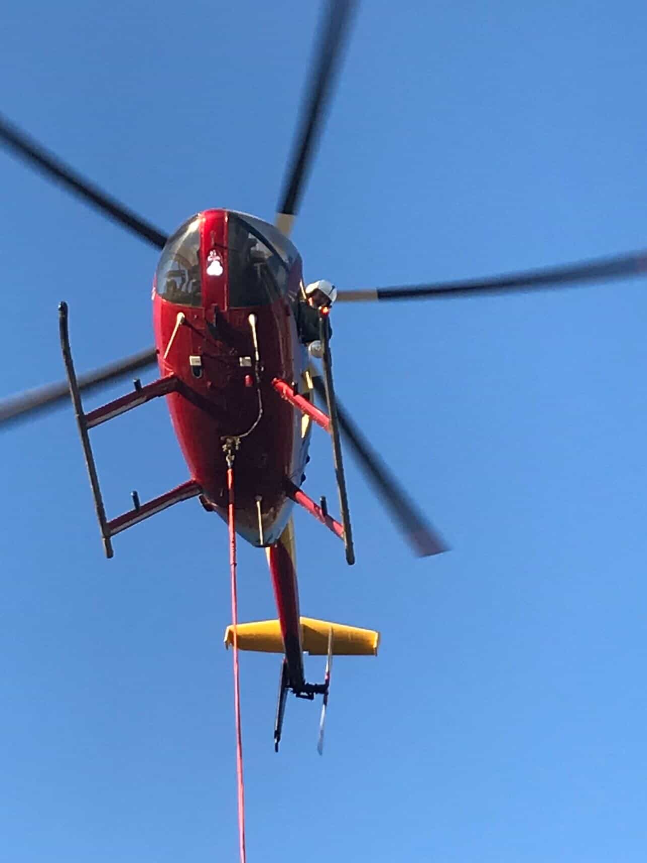 Red helicopter from the front with rotors spinning, longline attached