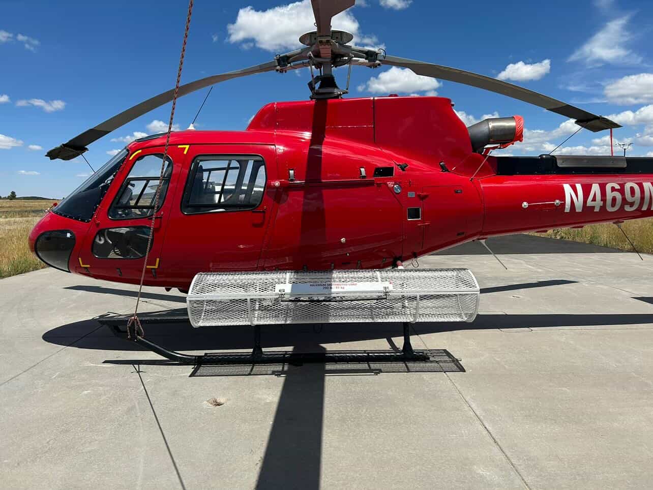 Red AS350 N469M on helipad with cargo basket attached to skids