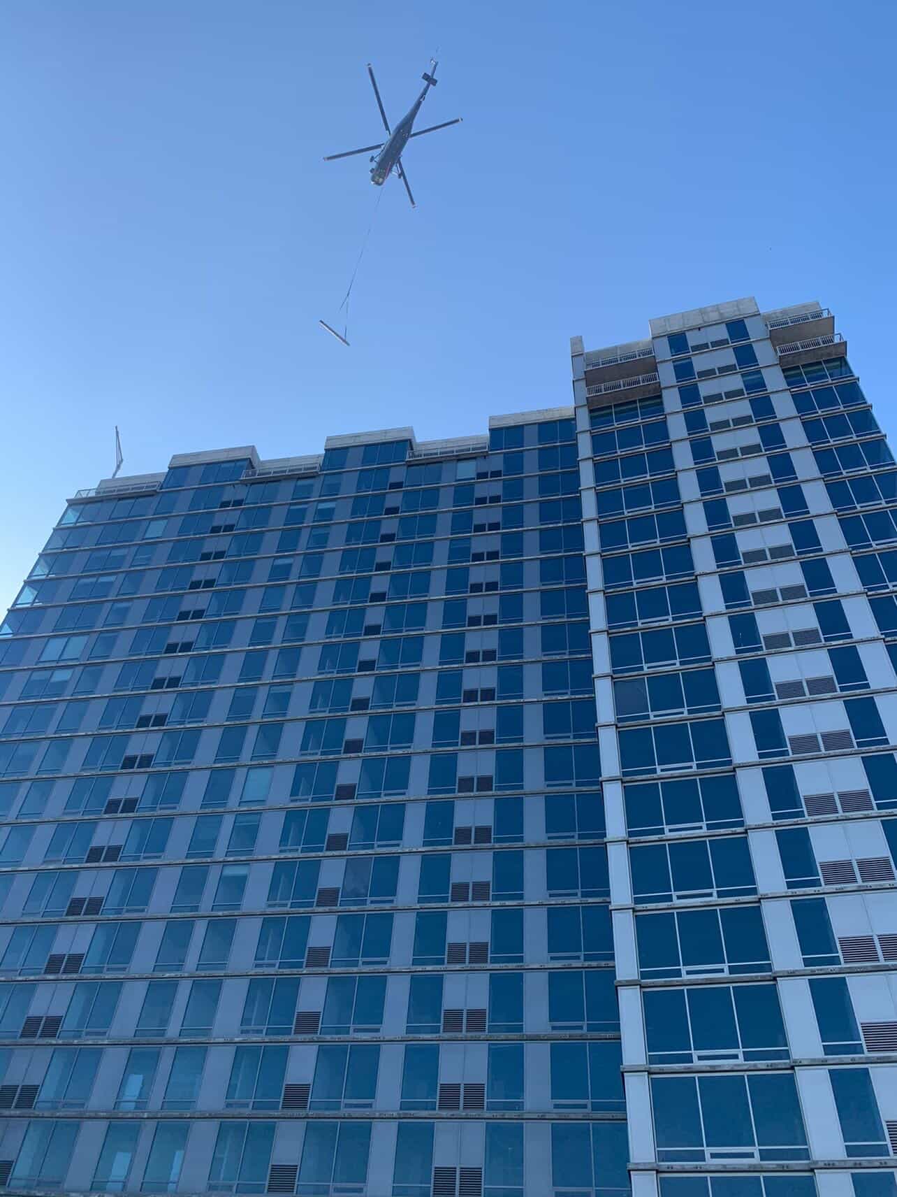 Helicopter performing rooftop lift over tall blue skyscraper