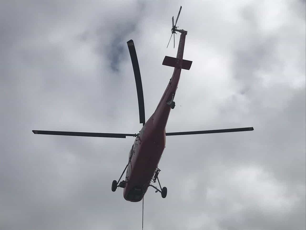Red Sikorsky helicopter viewed from below against overcast sky