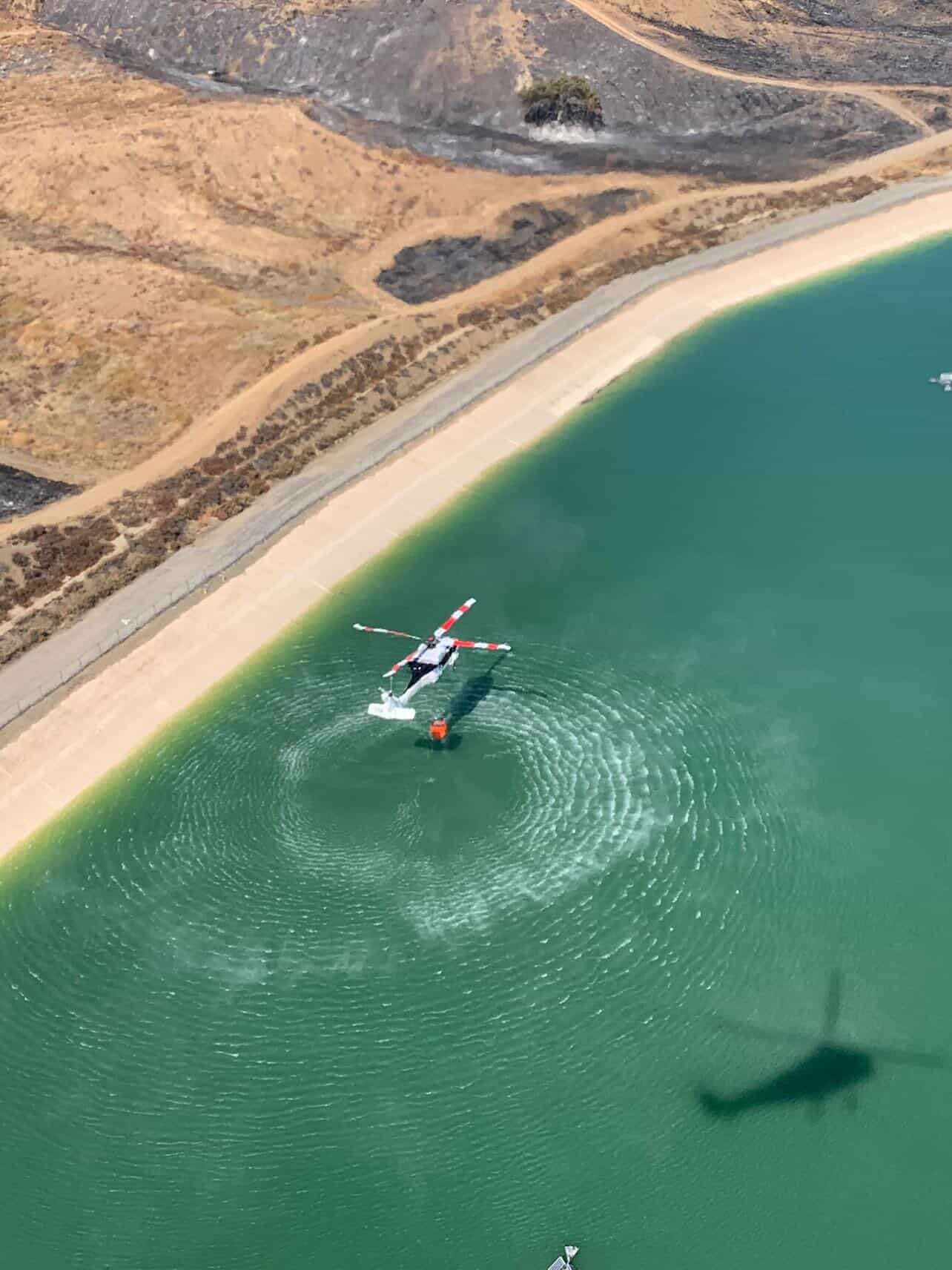 Aerial view of helicopter water-scooping from reservoir during fire response